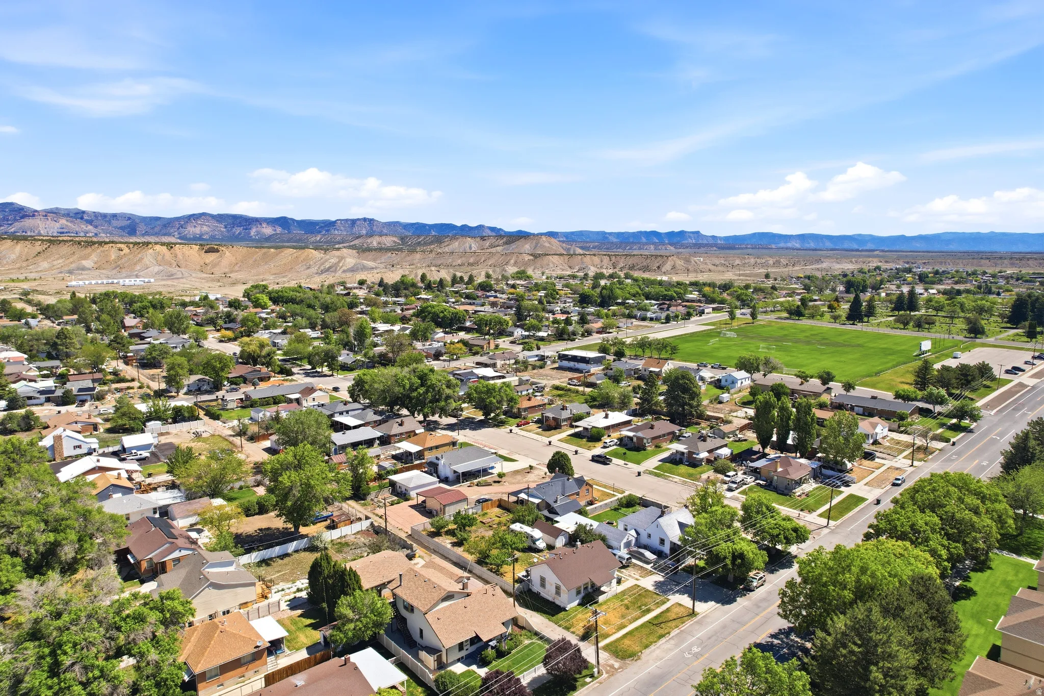 Expansive aerial perspective showcasing a residential area with varied home styles, mature tree canopies, open green spaces, and paved roads