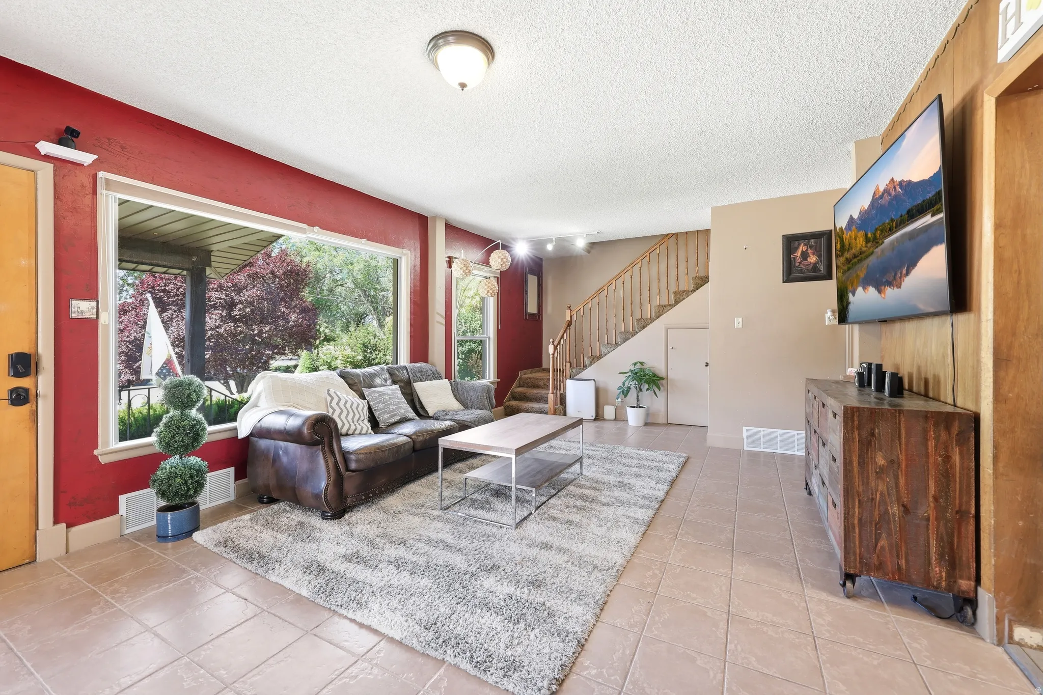 Spacious living area featuring large picture window, tile flooring, and a visible staircase