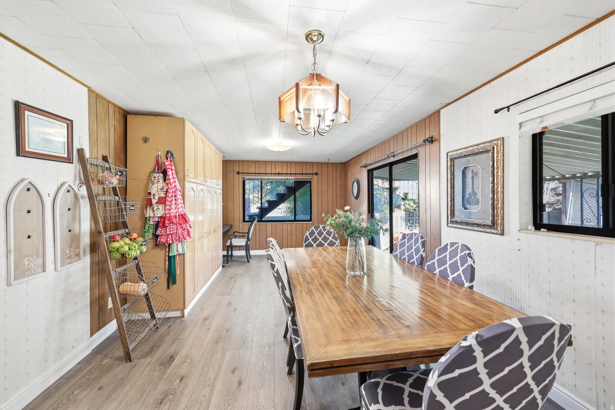 Dining area featuring wood-finish flooring, a decorative ceiling light fixture, paneled walls, and a window with a valance