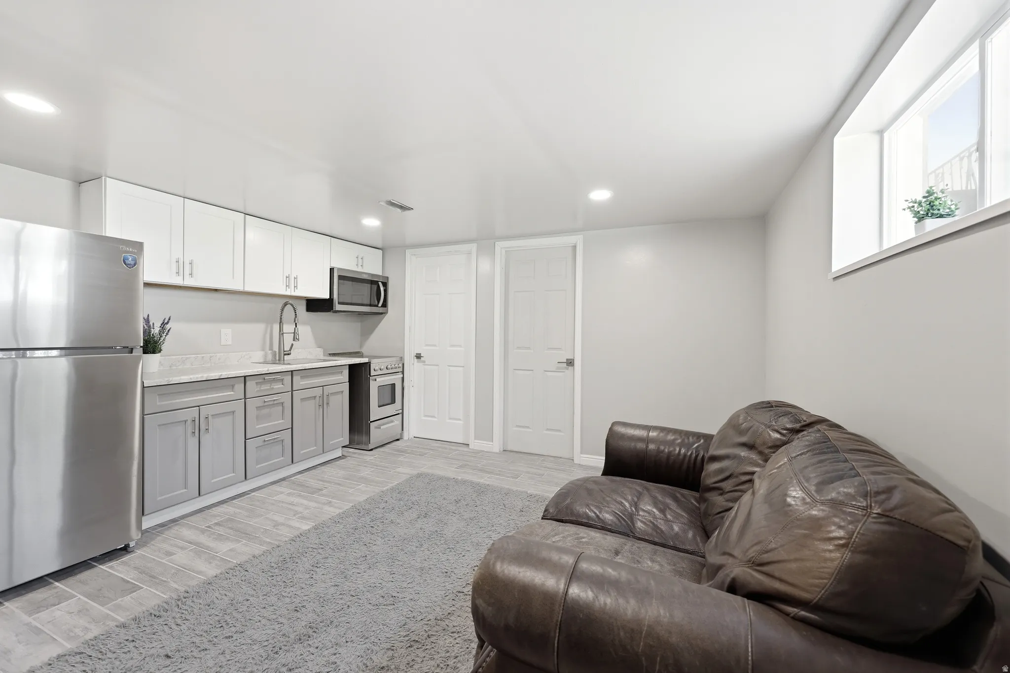 Open-concept living space featuring a compact kitchen with stainless steel appliances, two-tone cabinetry, and light-toned countertops
