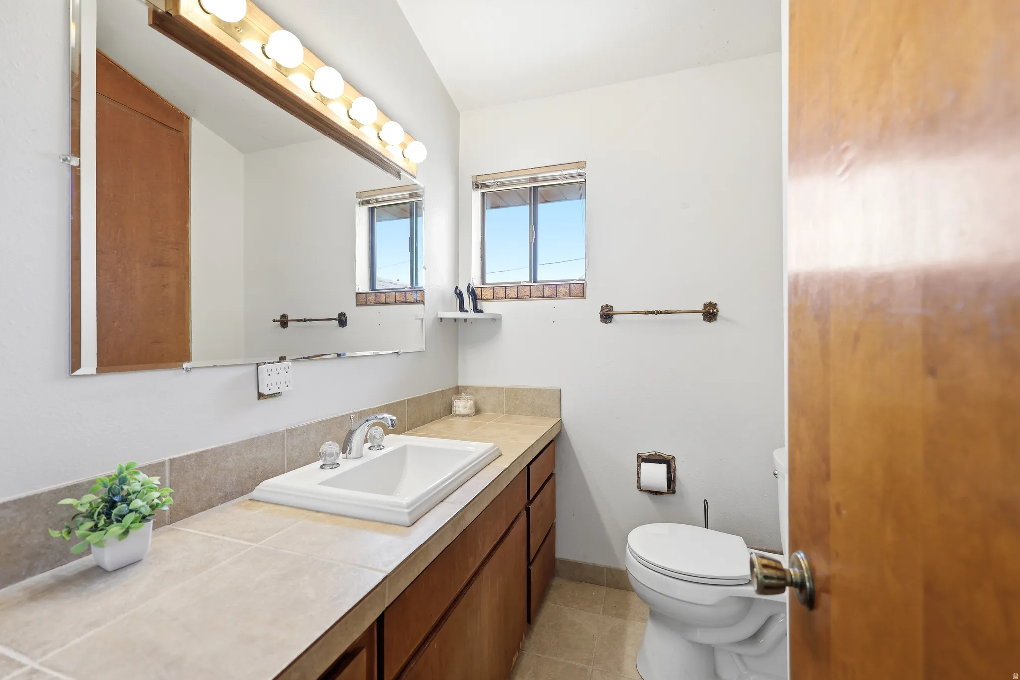 Bathroom featuring a rectangular drop-in sink, wood-finish cabinetry, neutral countertop, and a vanity mirror with overhead lighting