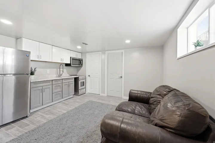 Open-concept living space featuring a compact kitchen with stainless steel appliances, two-tone cabinetry, and light-toned countertops