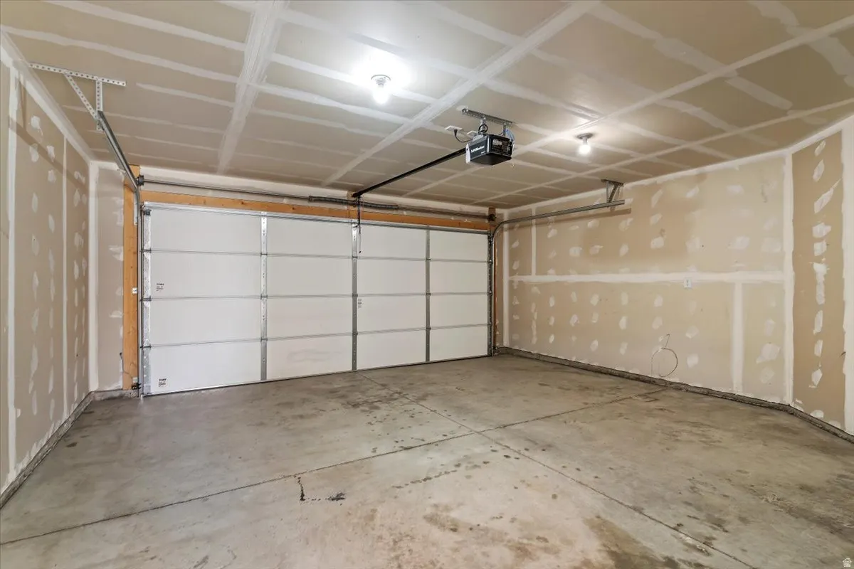 Spacious garage featuring a concrete floor, two overhead lights, and a white paneled garage door with an automatic opener