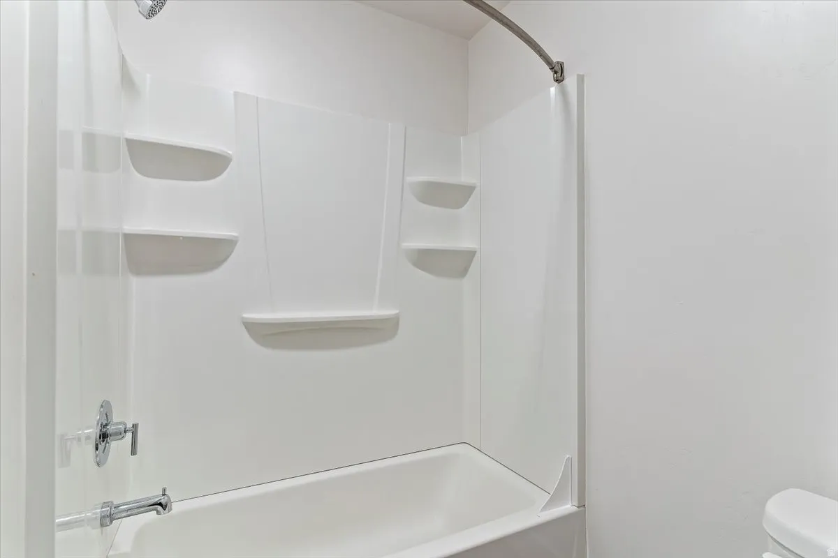 White bathtub with integrated wall panels featuring multiple built-in shelving units and a chrome shower head and faucet