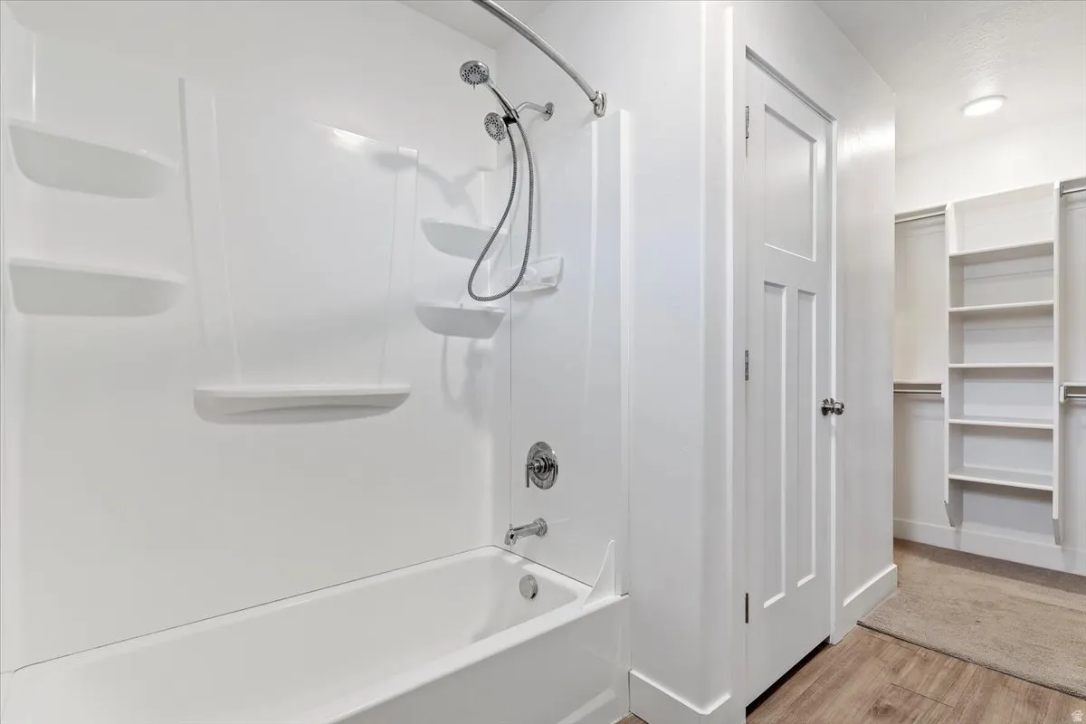 White acrylic tub and shower combination with chrome fixtures and integrated shelving