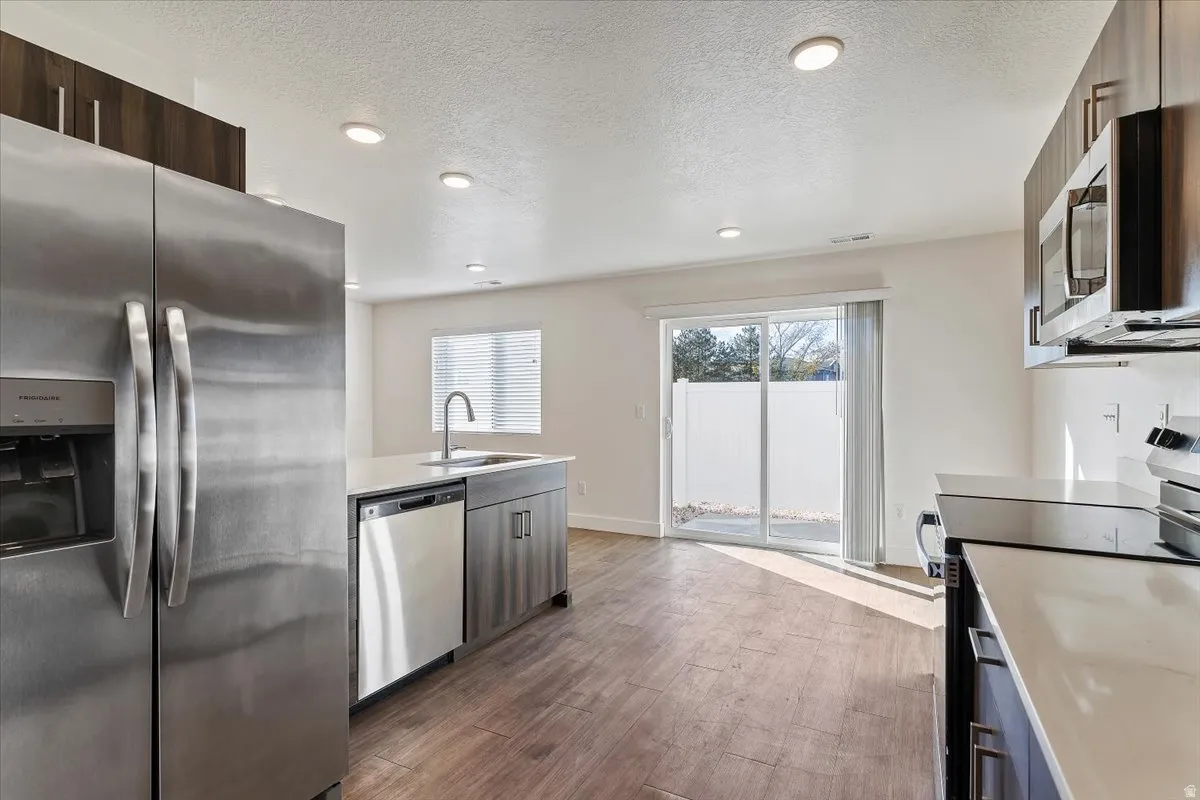 Modern kitchen featuring stainless steel appliances, wood-finish flooring, recessed lighting, white countertops, and contemporary cabinetry