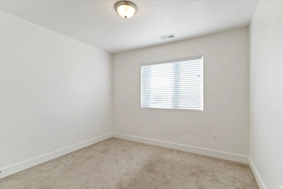 Bright interior space featuring a window with integrated blinds, neutral carpeting, white baseboards, and a flush-mount ceiling light fixture