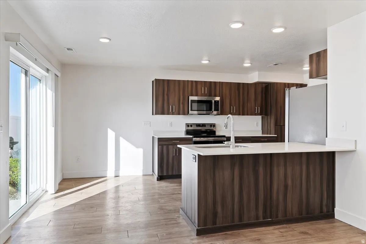 Open-concept kitchen featuring wood-grain cabinetry, stainless steel appliances, and a central island with a breakfast bar