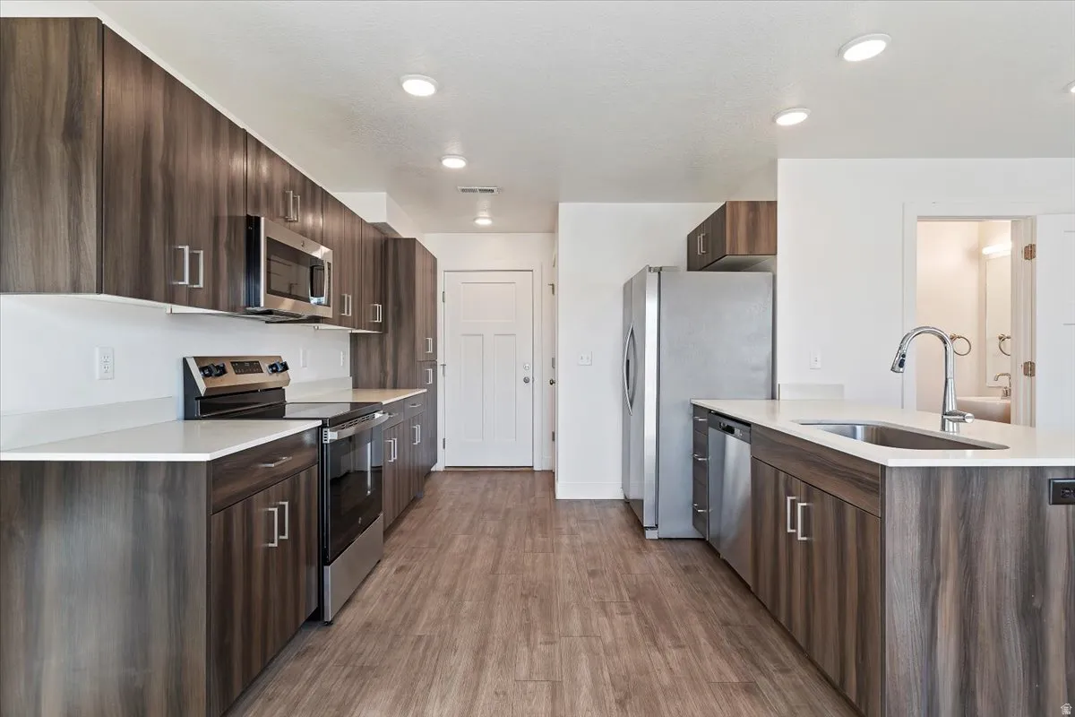 Modern kitchen featuring wood-finish cabinetry, stainless steel appliances, white countertops, recessed lighting, and wood-finish flooring