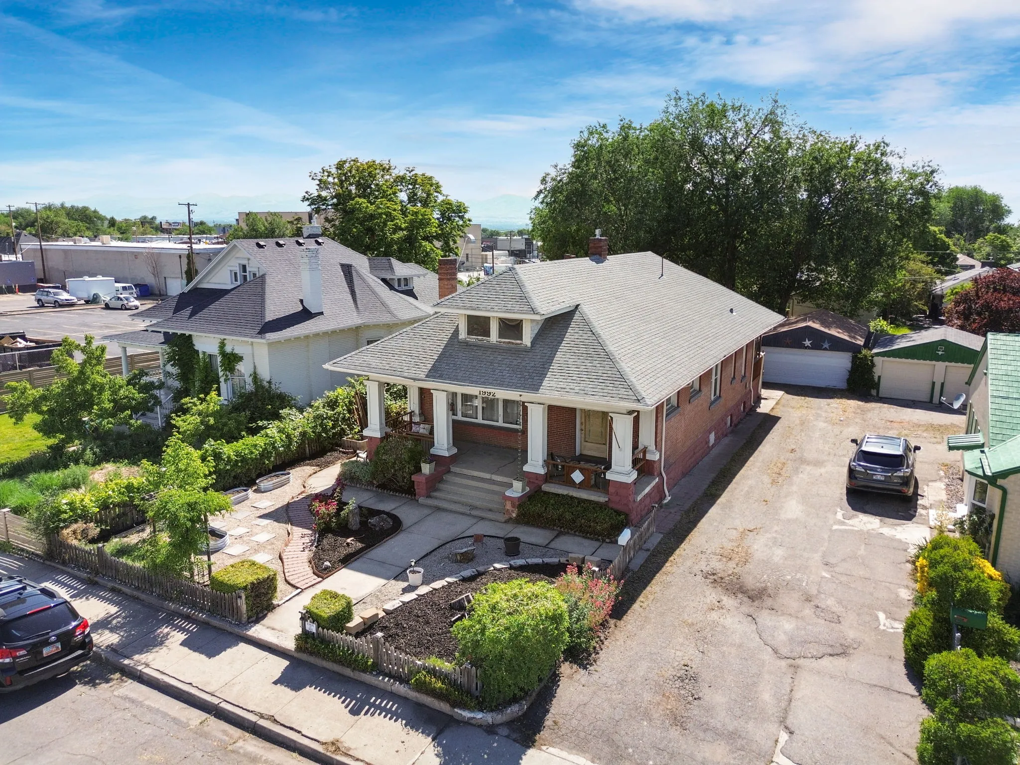 Brick exterior featuring a covered front porch with white pillars, a multi-car driveway, a detached garage, and a large front yard with mature landscaping and a brick pathway