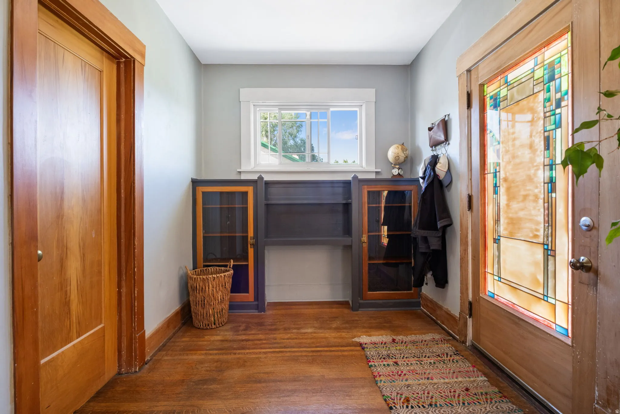 Entryway featuring wood-finish flooring, stained glass front door, built-in cabinetry, and a window with white trim