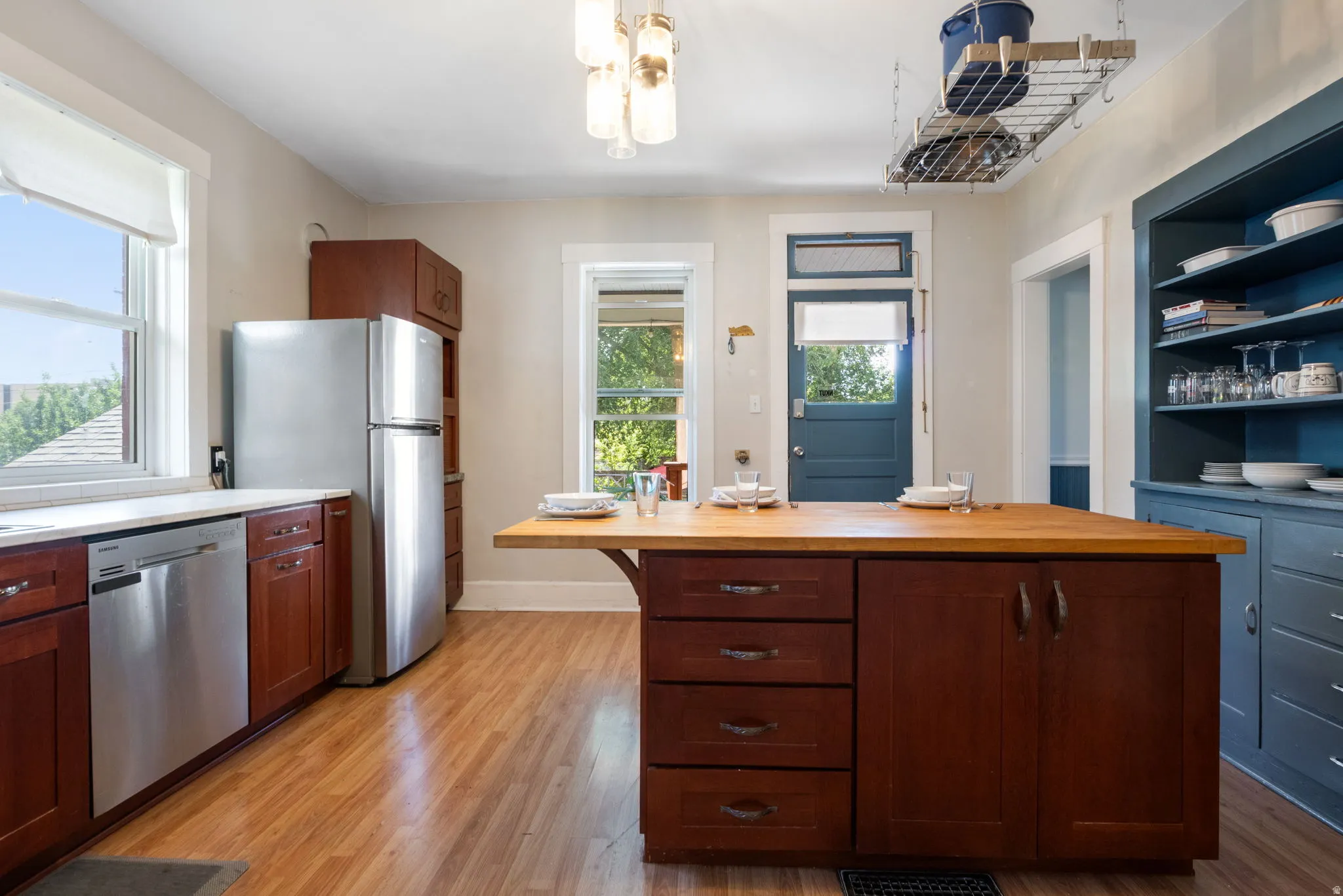 Kitchen featuring wood-finish flooring, stainless steel appliances including a refrigerator and dishwasher, dark wood cabinetry, and a kitchen island with an extended wood countertop