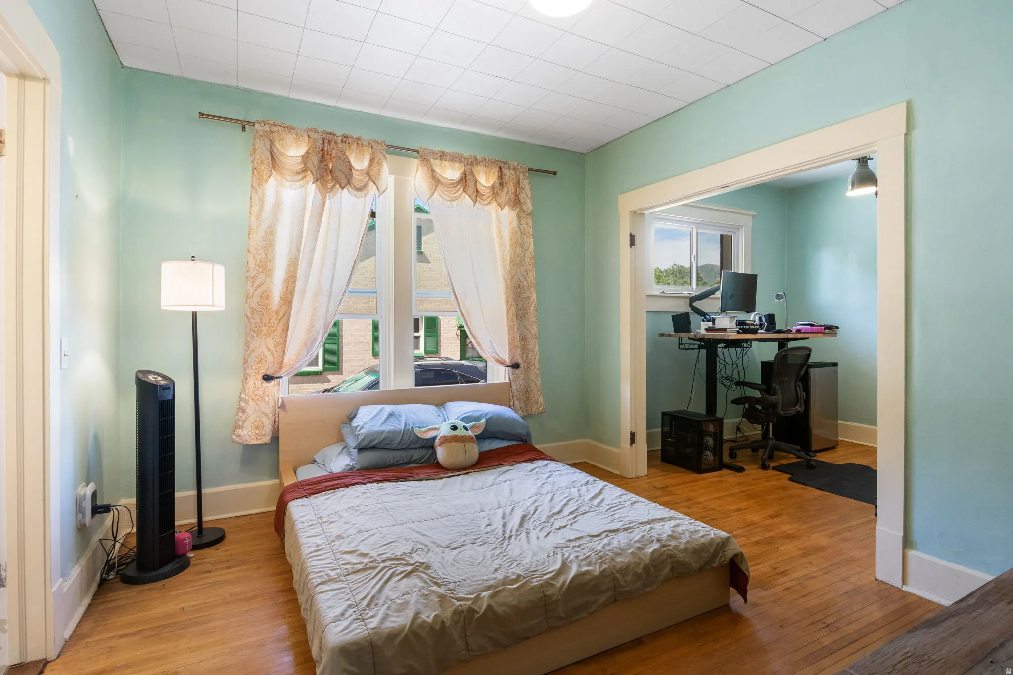 Room featuring wood-finish flooring, light blue walls, and a white grid-patterned ceiling
