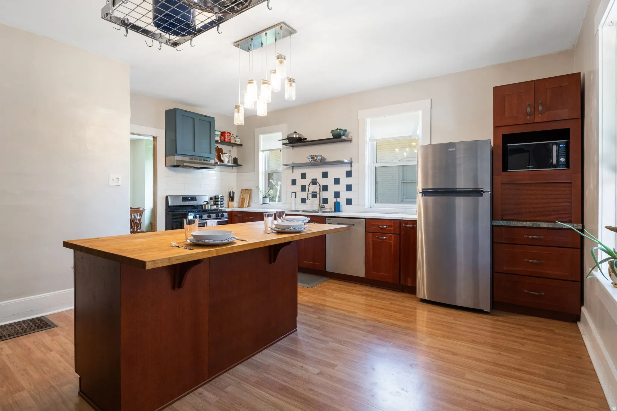 Kitchen featuring a central island with a wood-finish countertop, wood-finish flooring, stainless steel appliances, and a mosaic tile backsplash