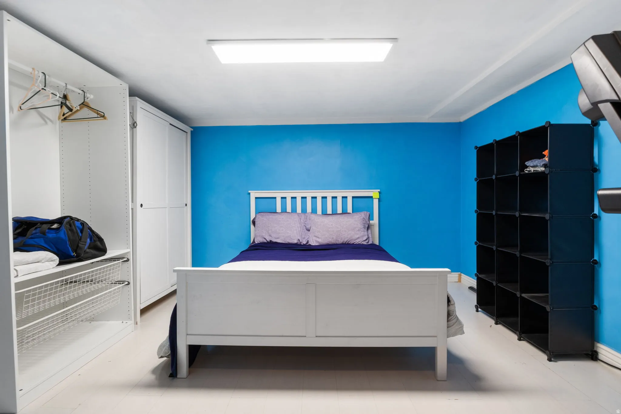 Room featuring white wood-finish flooring, a vibrant blue accent wall, and recessed ceiling lighting
