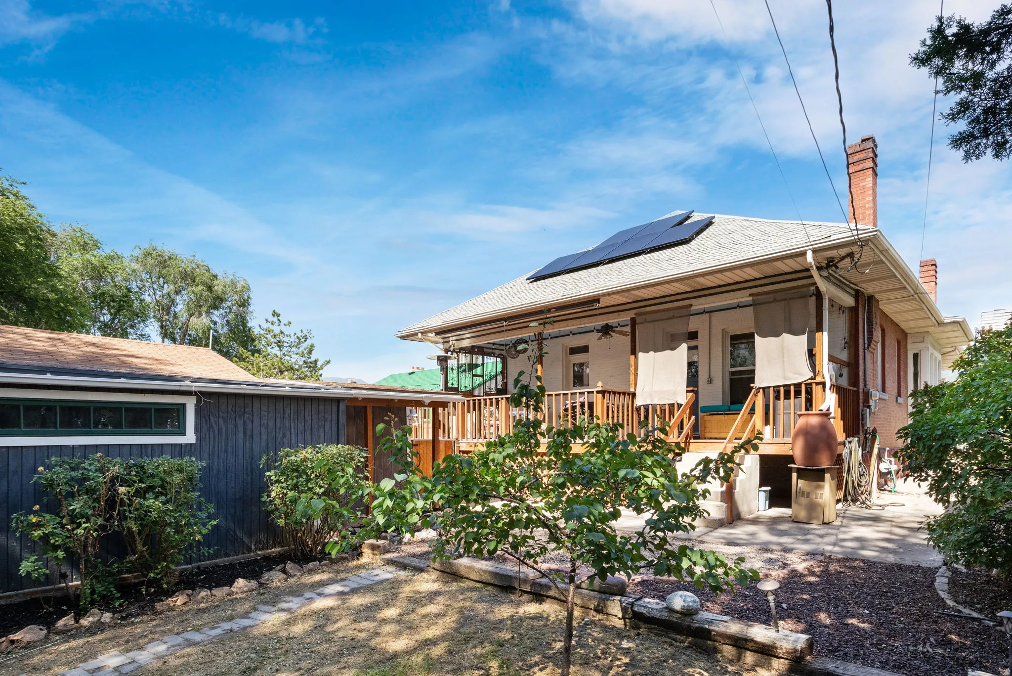 Rear exterior featuring an elevated wood deck, solar panels on the roof, and a brick chimney