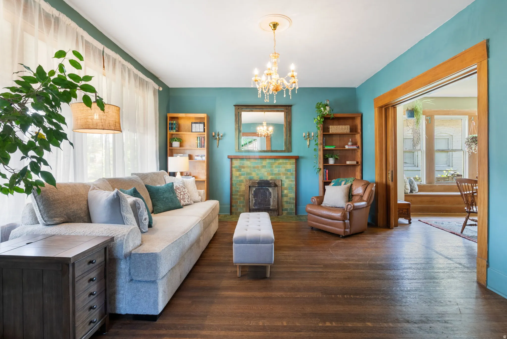 Spacious living area featuring wood-finish flooring, a decorative fireplace with green tiled surround, and a chandelier light fixture