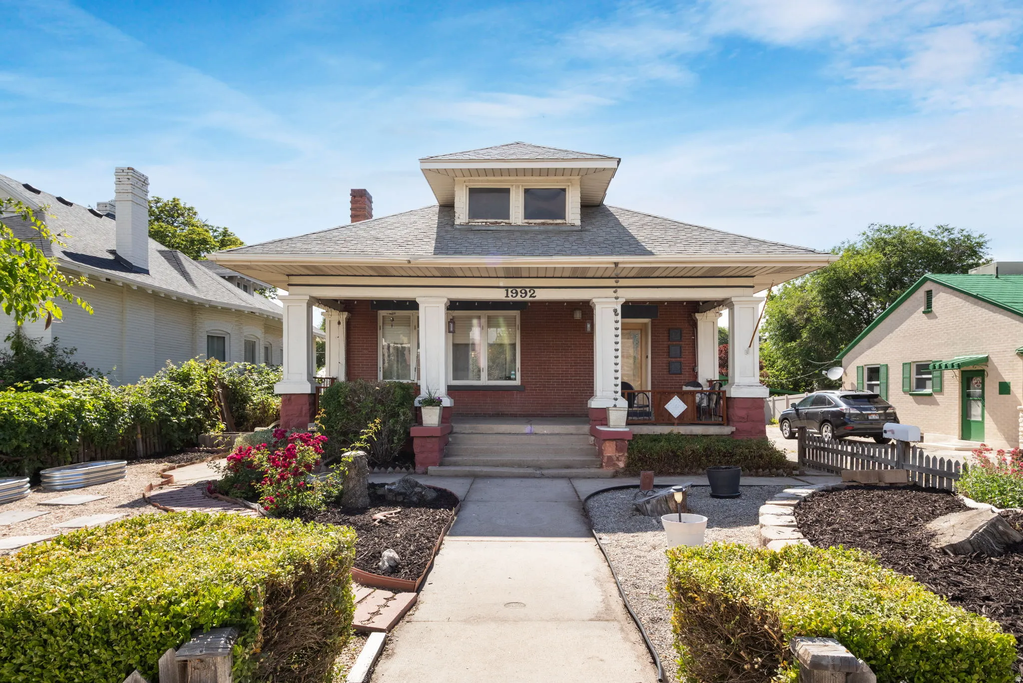 Brick residence featuring a covered front porch with white columns, a dormer window, and mature landscaping