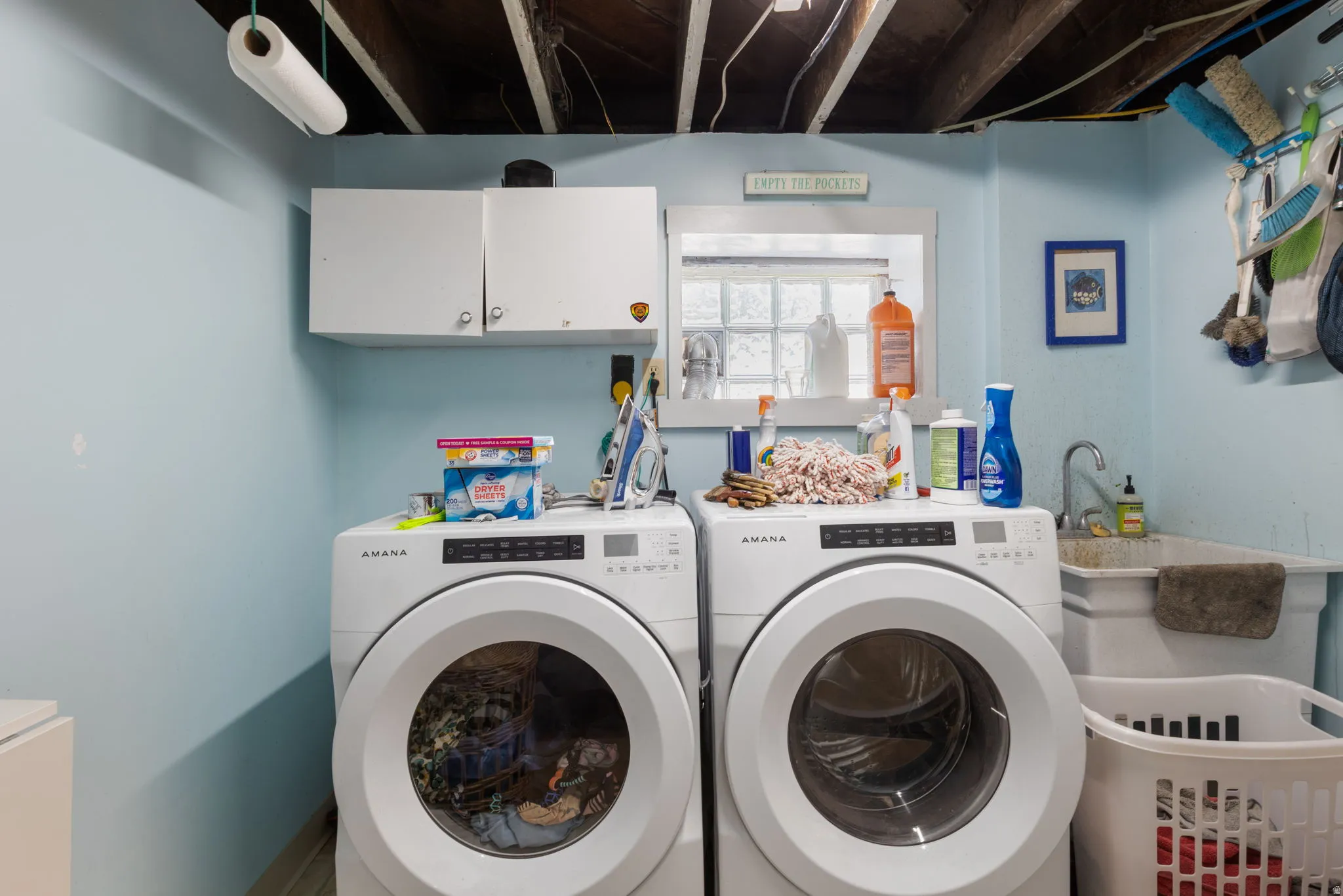 Dedicated laundry area featuring front-loading appliances, a built-in utility sink with a faucet, upper cabinetry, and a window providing natural illumination