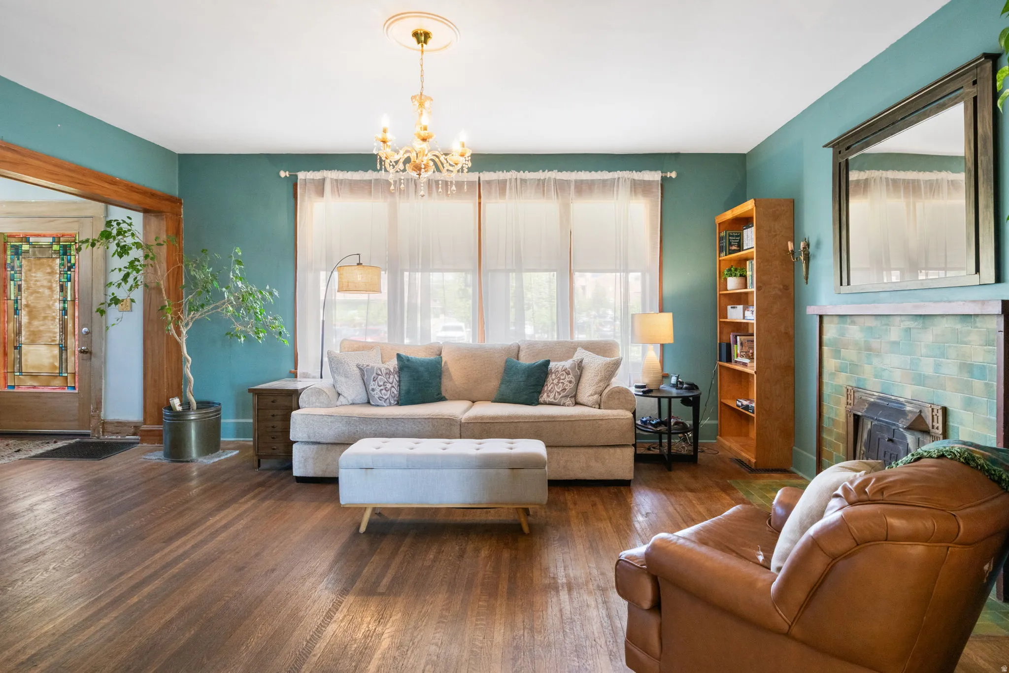 Living area featuring wood-finish flooring, a fireplace with tiled surround, a chandelier, and a decorative stained-glass entry door