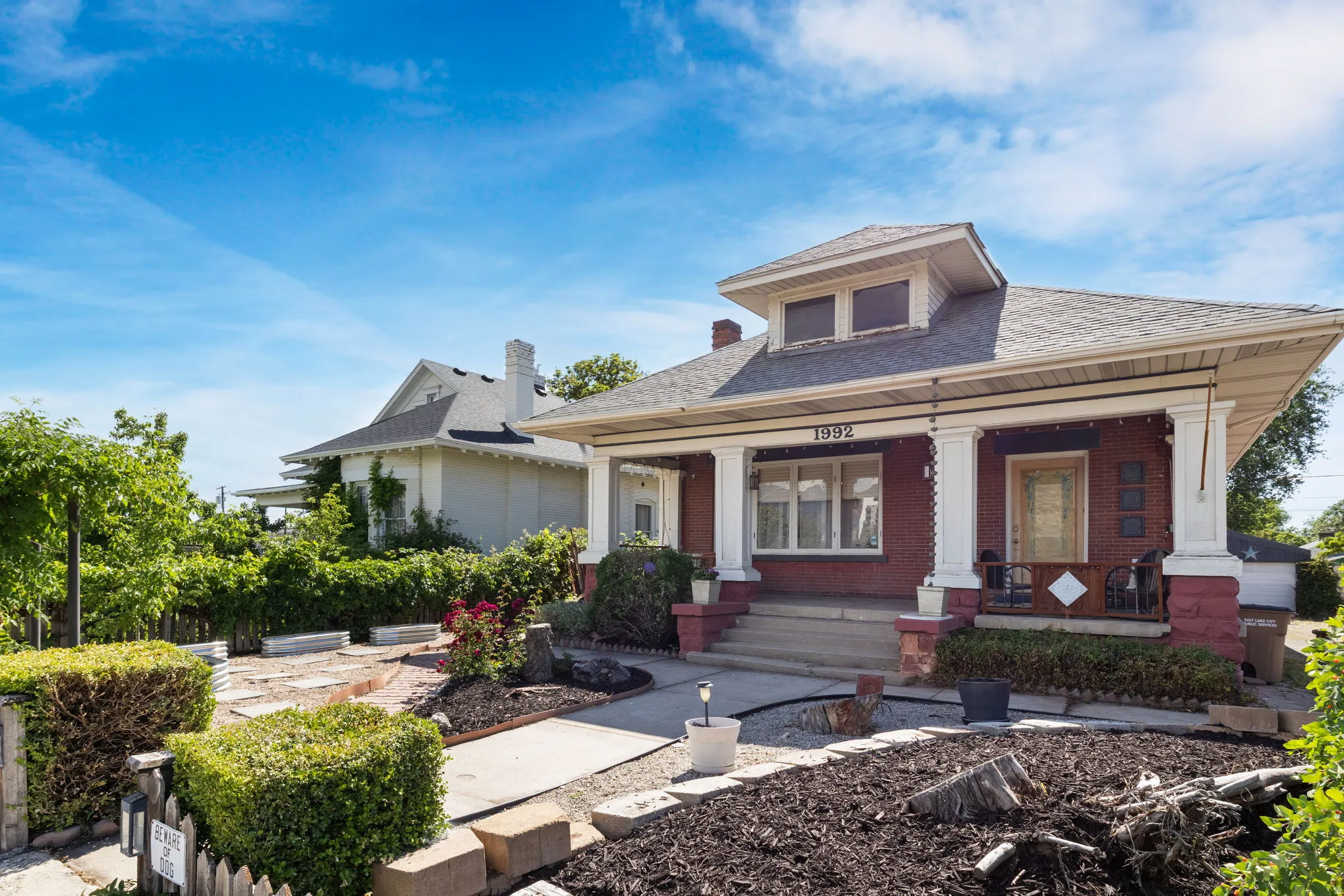 Brick bungalow featuring a covered front porch with substantial columns, a dormer window, and stone-clad foundation