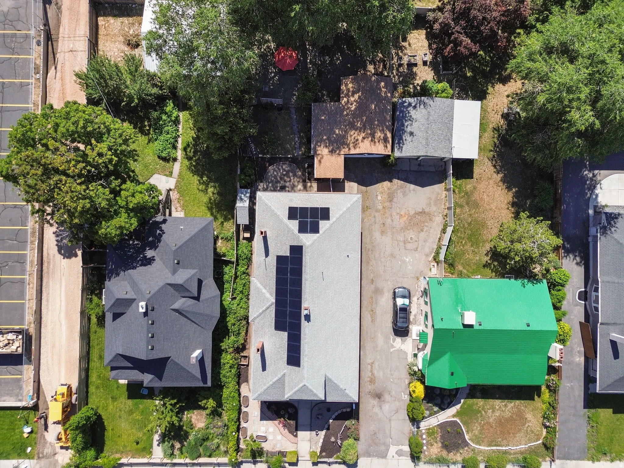 Aerial view showcasing a property with a grey shingle roof featuring solar panels, a paved driveway, and mature landscaping