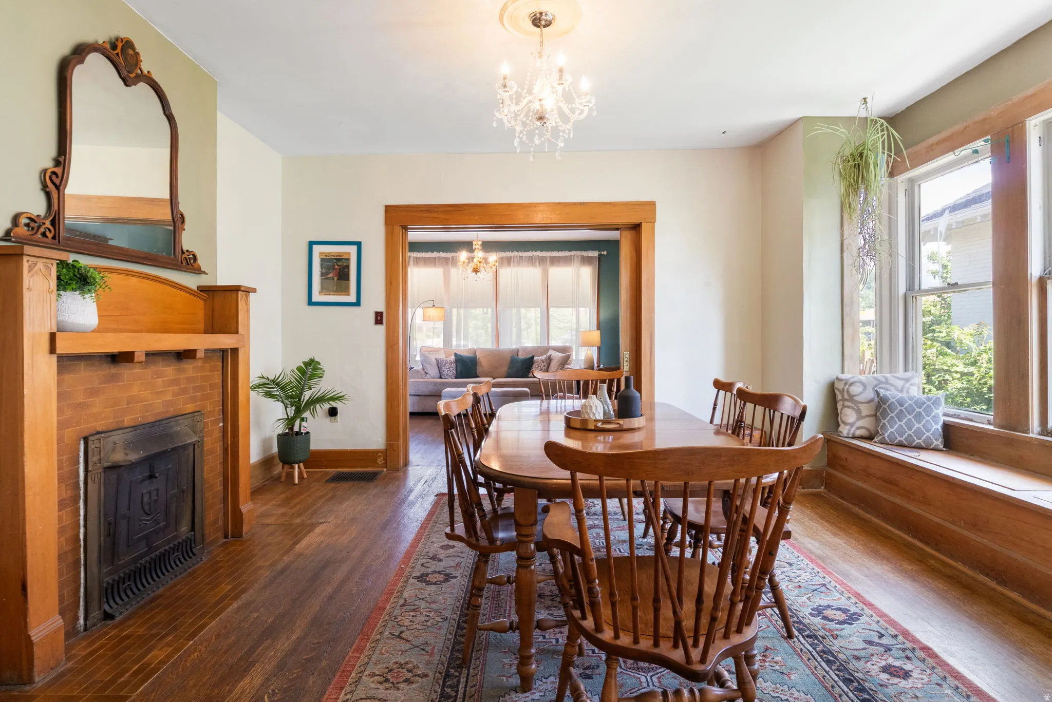 Formal dining area featuring rich wood-finish flooring, a brick fireplace with a wood mantle, a built-in window bench, a decorative chandelier, and broad architectural trim around the doorway