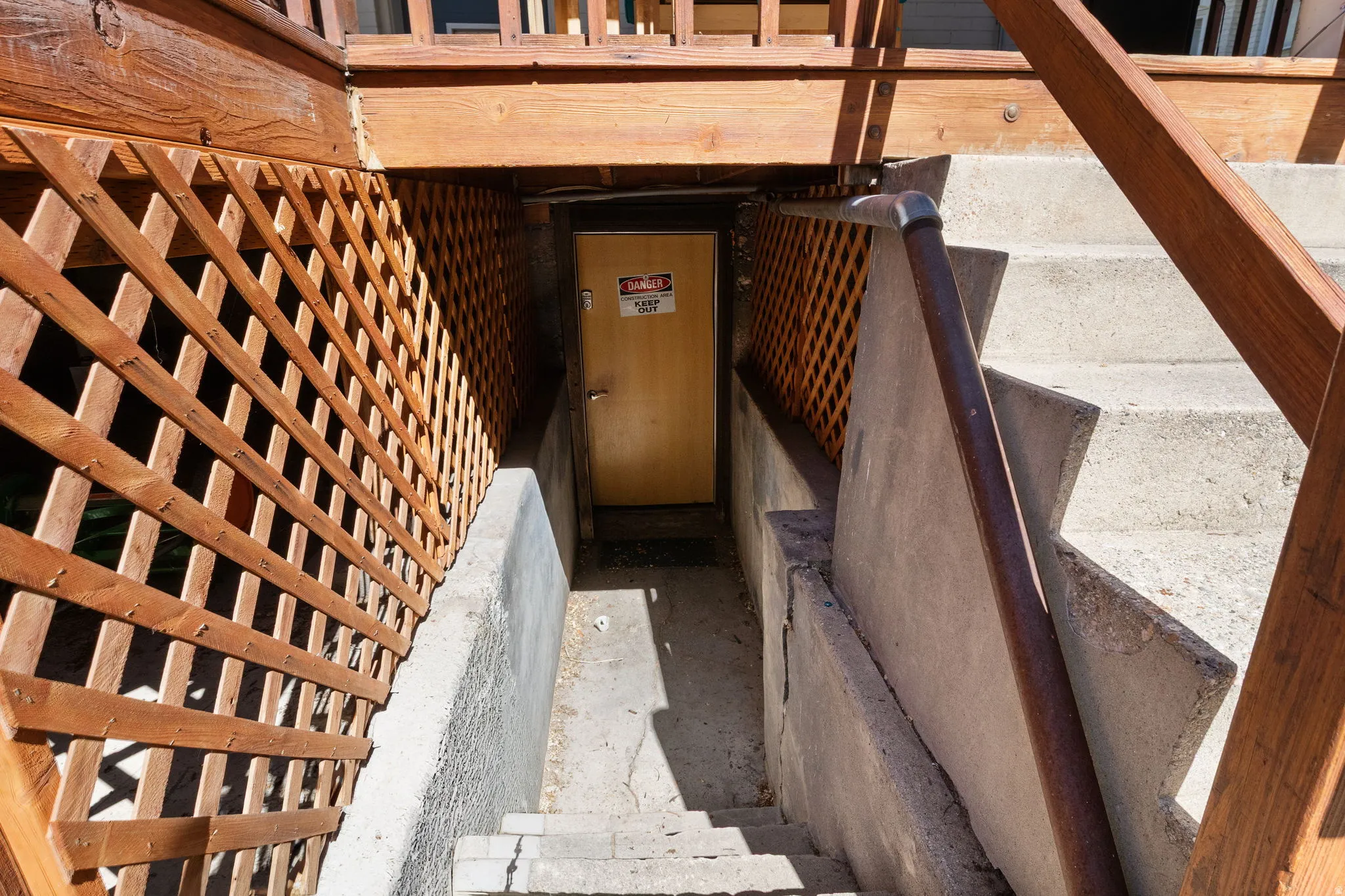Concrete staircase descending to a yellow door, framed by wood lattice and a wood handrail