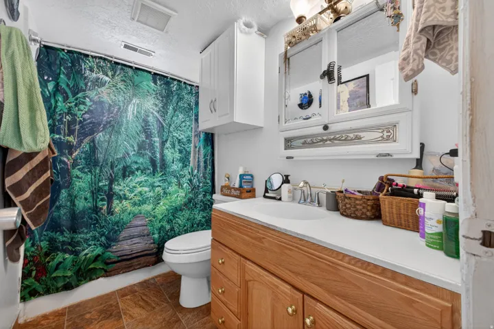 Bathroom featuring a single vanity with a white countertop and wood-finish cabinetry, a wall-mounted medicine cabinet with decorative accents, and tiled flooring