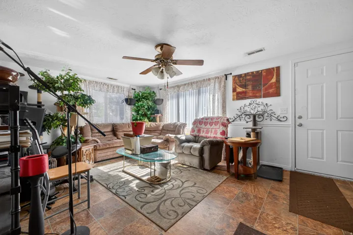 Spacious living area featuring a ceiling fan, recessed lighting, and large windows with vertical blinds