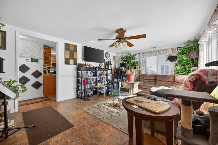 Living area featuring wood-finish flooring, a ceiling fan with integrated lighting, and a window with valance