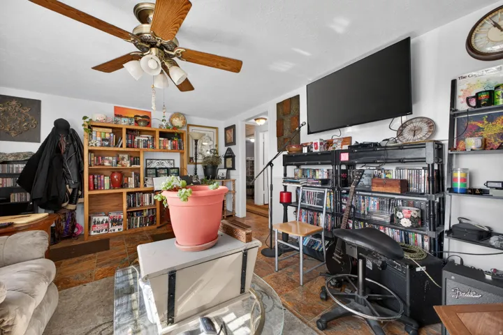 Living area featuring wood-finish flooring, a ceiling fan with light fixture, built-in shelving, and a wall-mounted display