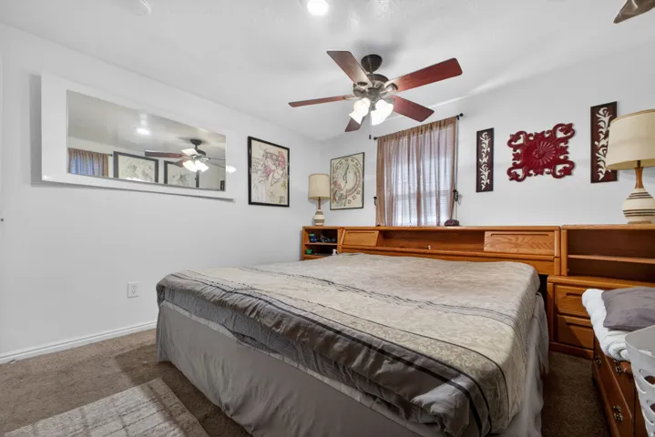Carpeted room featuring a built-in wooden headboard with integrated shelving and storage, a ceiling fan with light fixture, and a window with sheer curtains