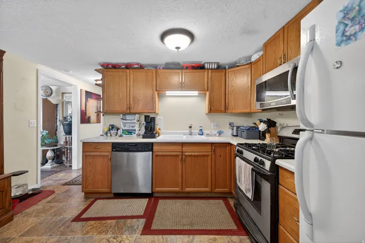 Kitchen featuring wood cabinetry, light countertops, stainless steel dishwasher, stainless steel microwave, and a gas range
