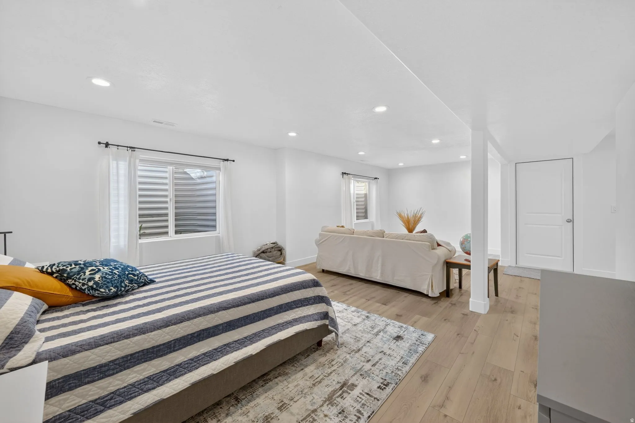 Spacious room with light wood-finish flooring, recessed lighting, and a white paneled door