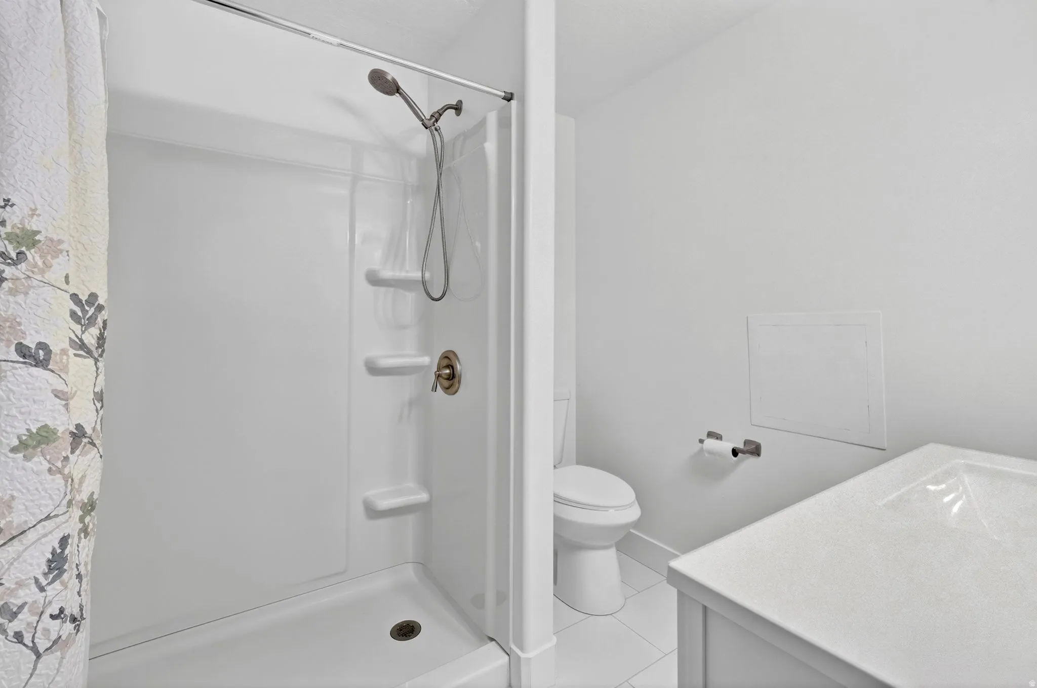 Bathroom featuring a white shower with an adjustable showerhead, built-in shelving, a white toilet, and a vanity with an integrated sink and light-colored countertop