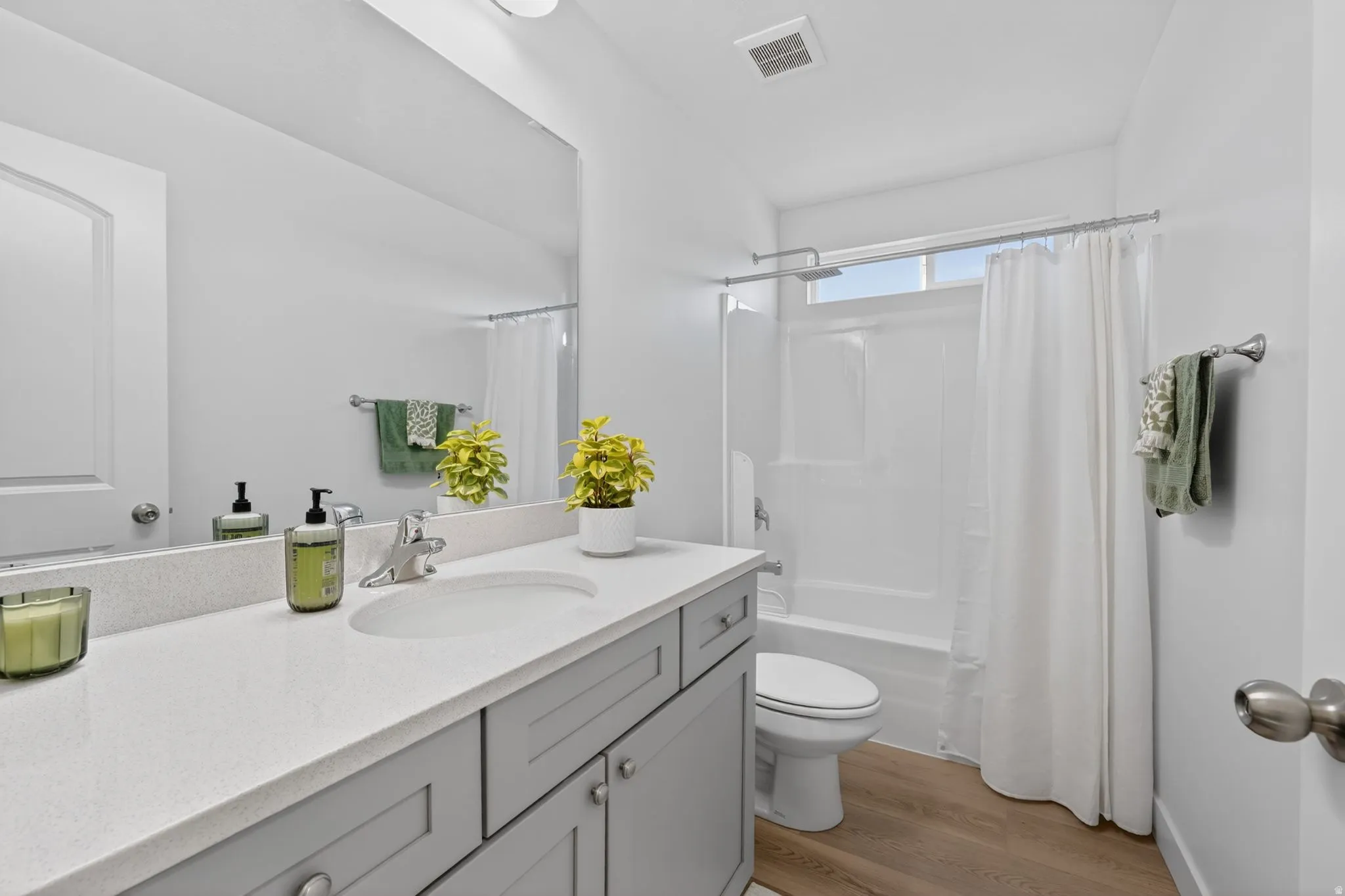 Bathroom featuring a light gray vanity with an integrated white sink, a large mirror, a white toilet, and a white shower/tub combination