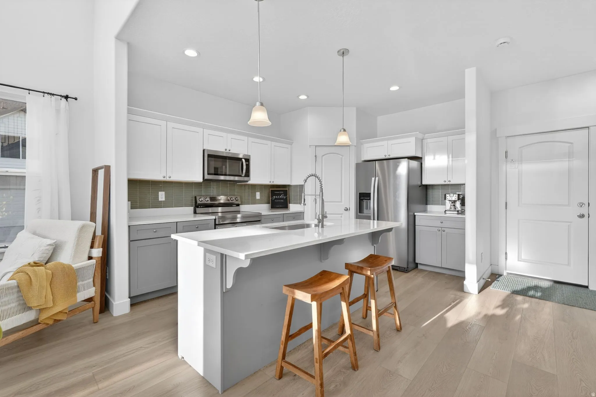 Contemporary kitchen featuring an island with seating, stainless steel appliances, white cabinetry, a green subway tile backsplash, and light wood-finish flooring