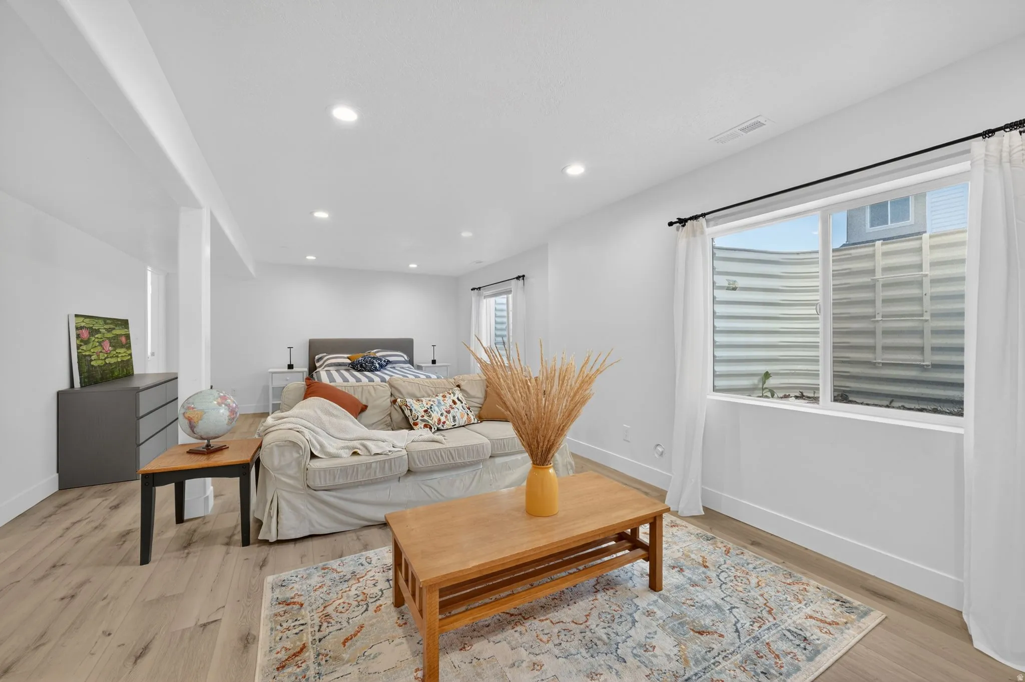Open-concept space featuring light wood-finish flooring, recessed lighting, a white window frame with white curtains, and white walls