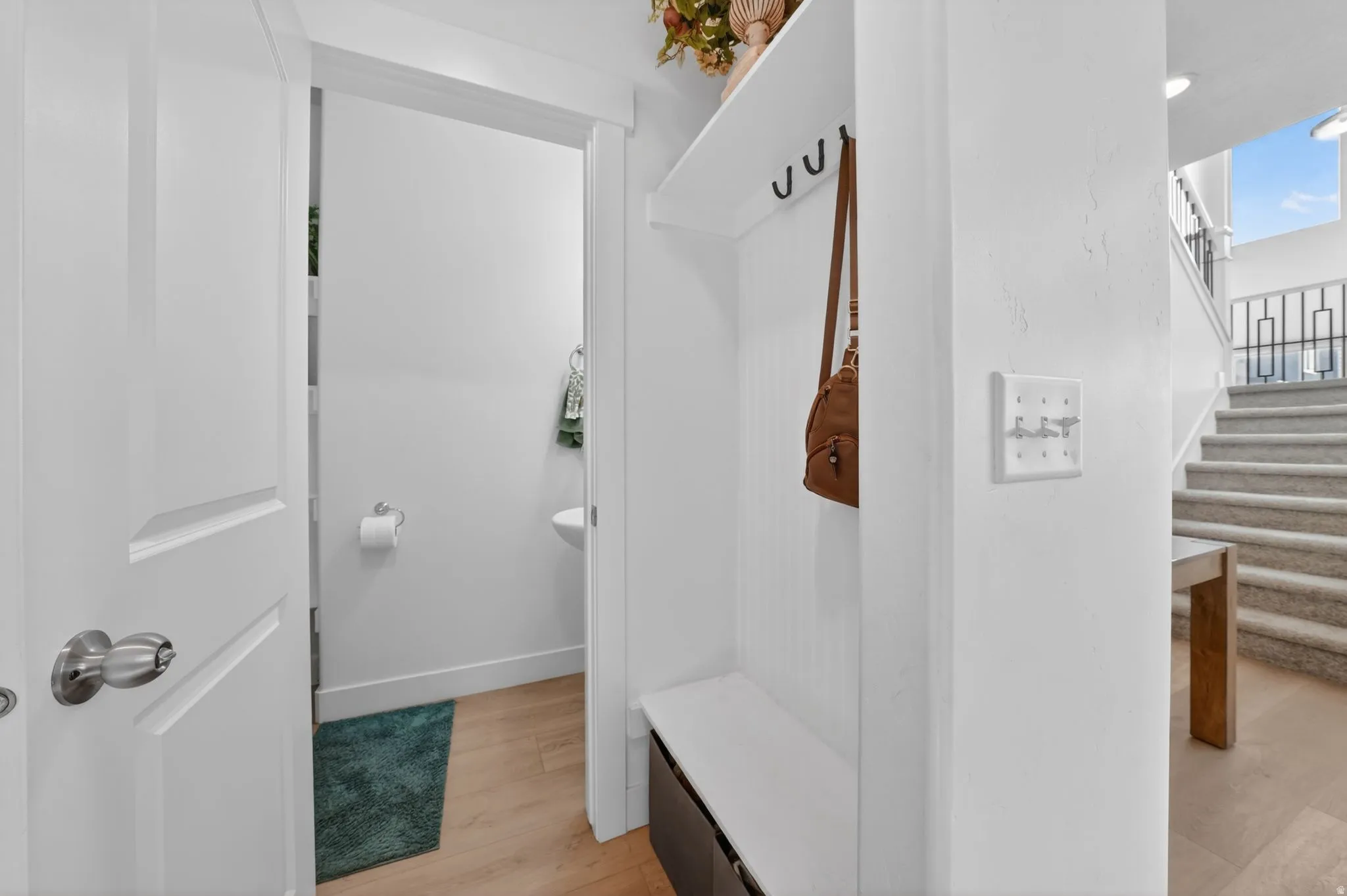 Entryway with built-in bench and coat hooks, leading to a powder room with a pedestal sink and toilet