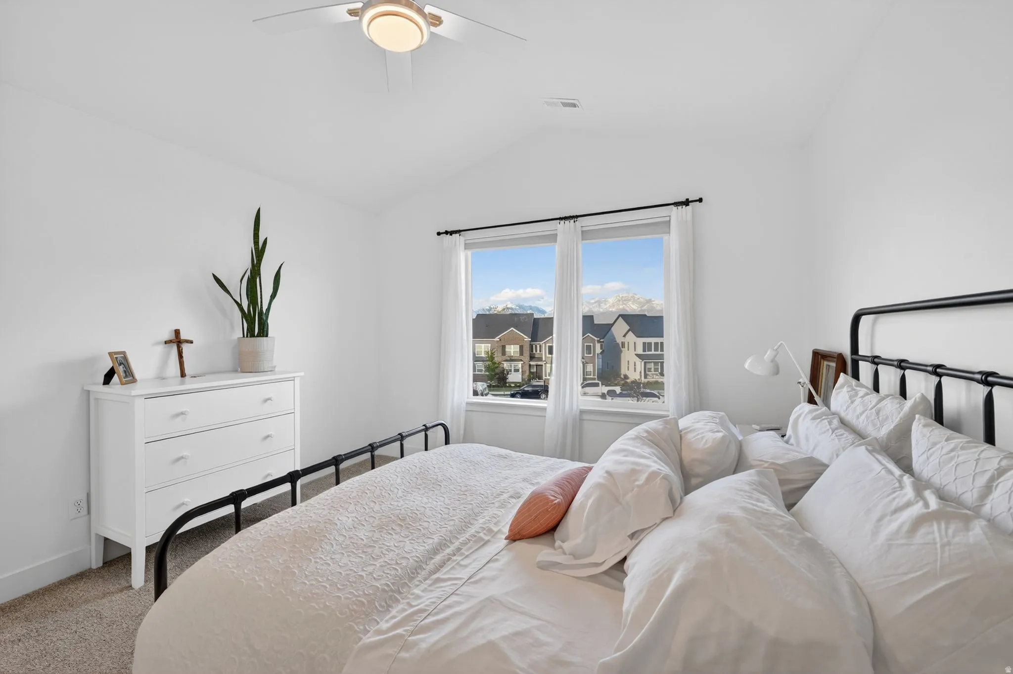Bright bedroom featuring a vaulted ceiling with a flush-mount ceiling fan, neutral carpet flooring, and a large window with mountain scenery