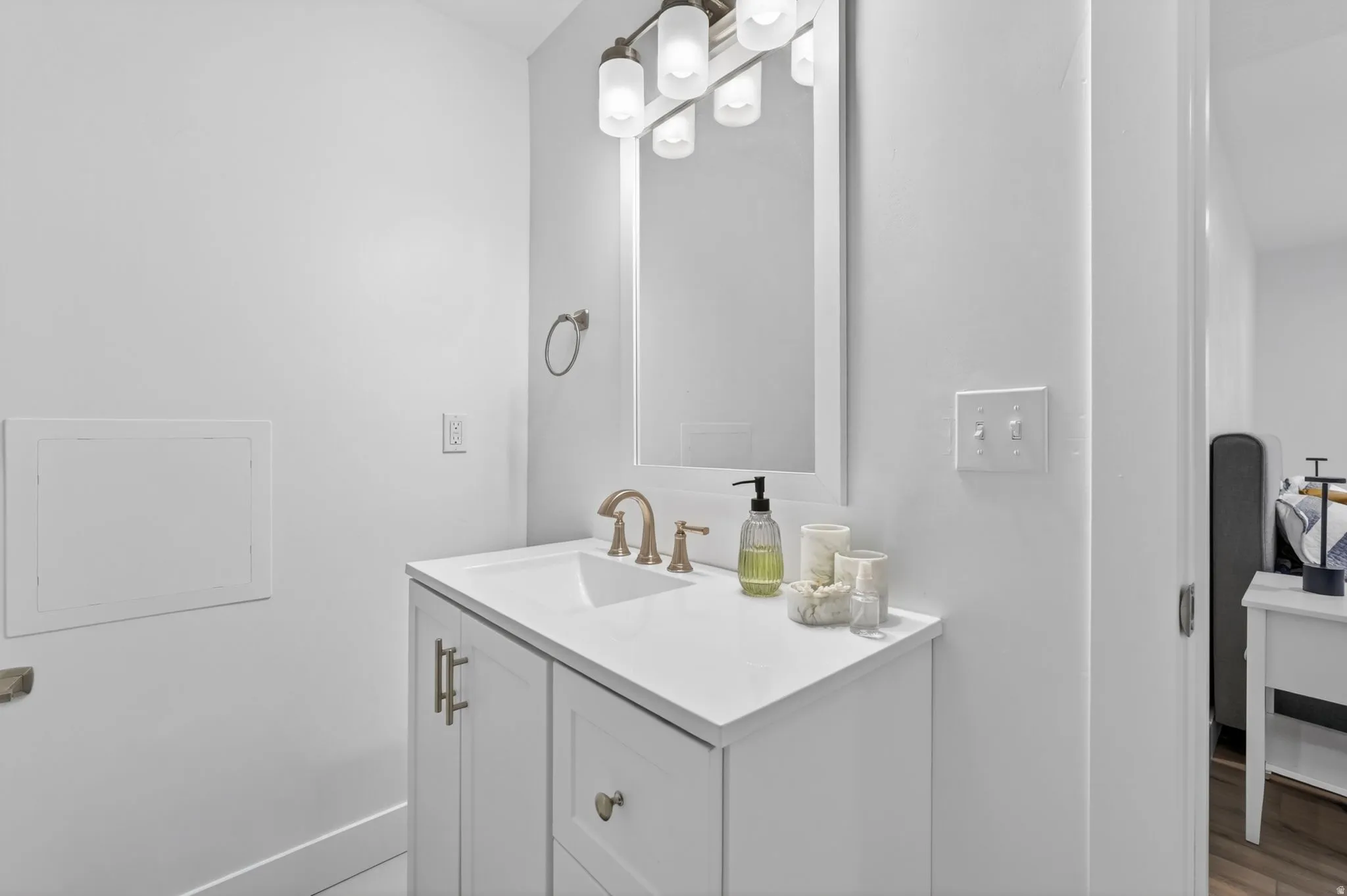 Bathroom vanity featuring white cabinetry with brushed gold hardware, a white countertop, and an undermount sink