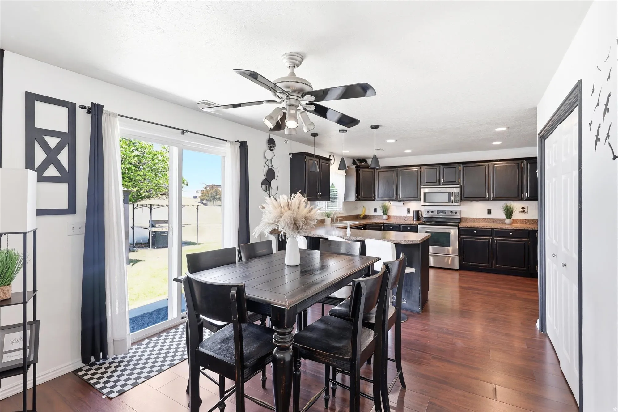 Open-concept kitchen and dining area featuring dark wood-finish flooring, a ceiling fan with integrated lighting, and white walls