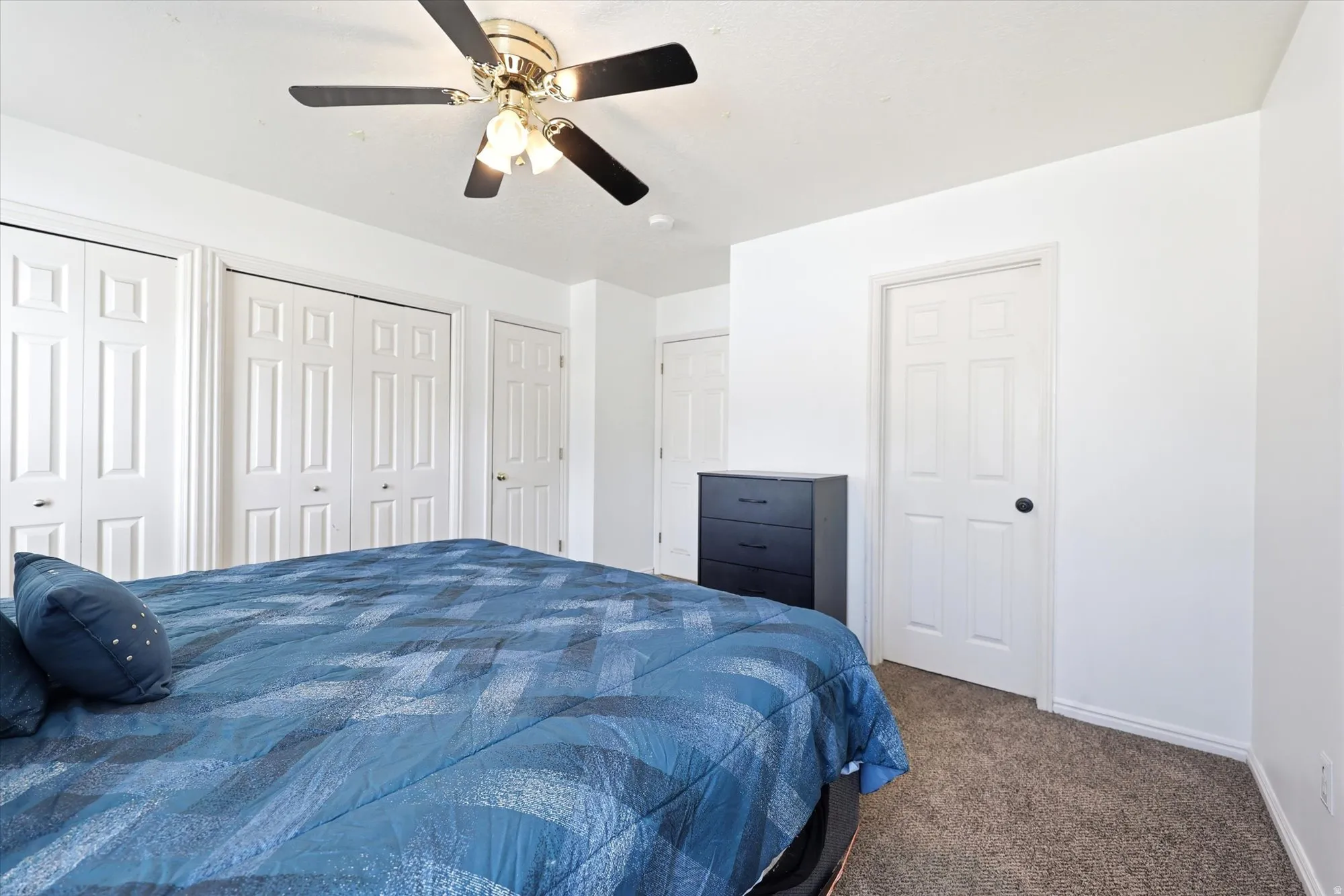 Spacious room featuring neutral carpet flooring, white walls, multiple panel doors, and a ceiling fan with integrated lighting