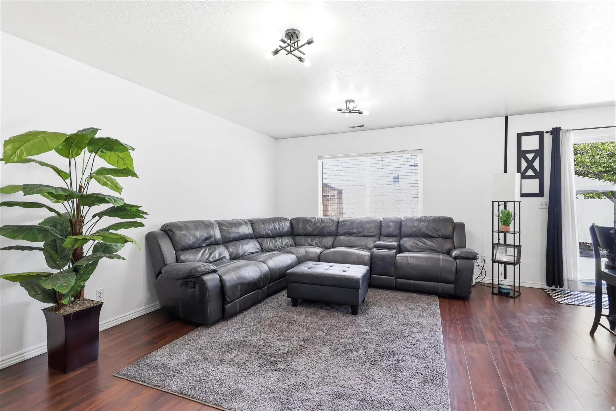 Spacious living area featuring rich wood-finish flooring, white painted walls, and contemporary ceiling light fixtures