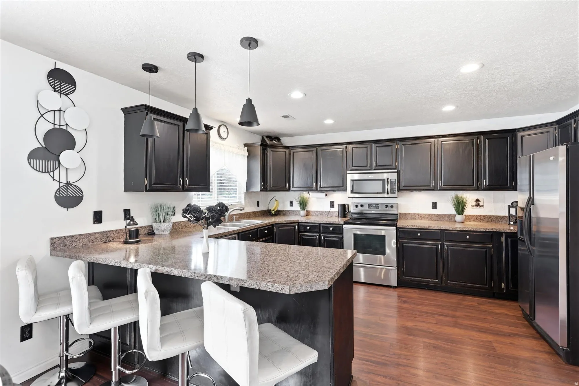 Kitchen featuring dark wood cabinetry, stainless steel appliances, speckled stone countertops, and wood-finish flooring