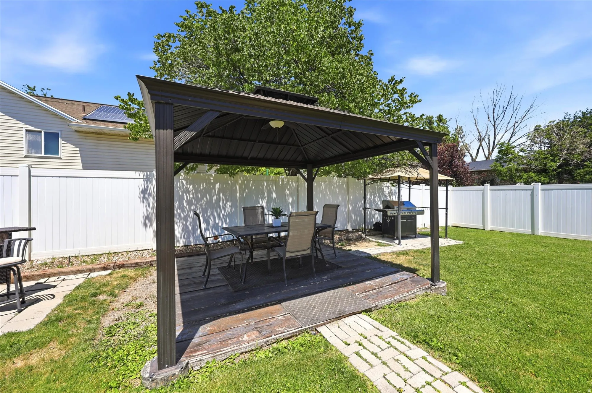 Outdoor patio featuring a black metal gazebo with a built-in light fixture, a wood-finish deck, and a paver stone pathway
