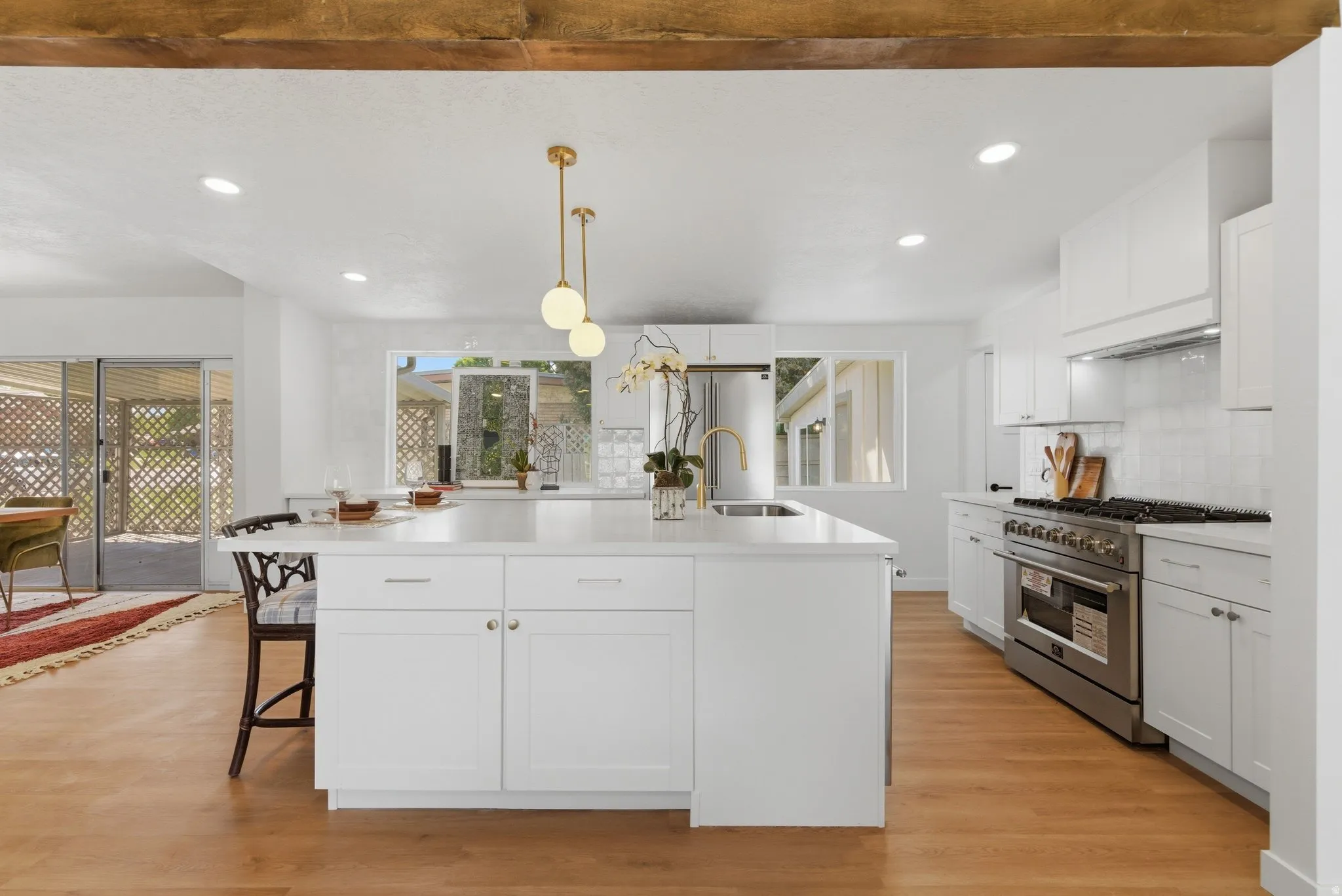 Modern kitchen featuring a large central island with seating, white shaker cabinetry, stainless steel appliances including a range with a hood, and wood-finish flooring