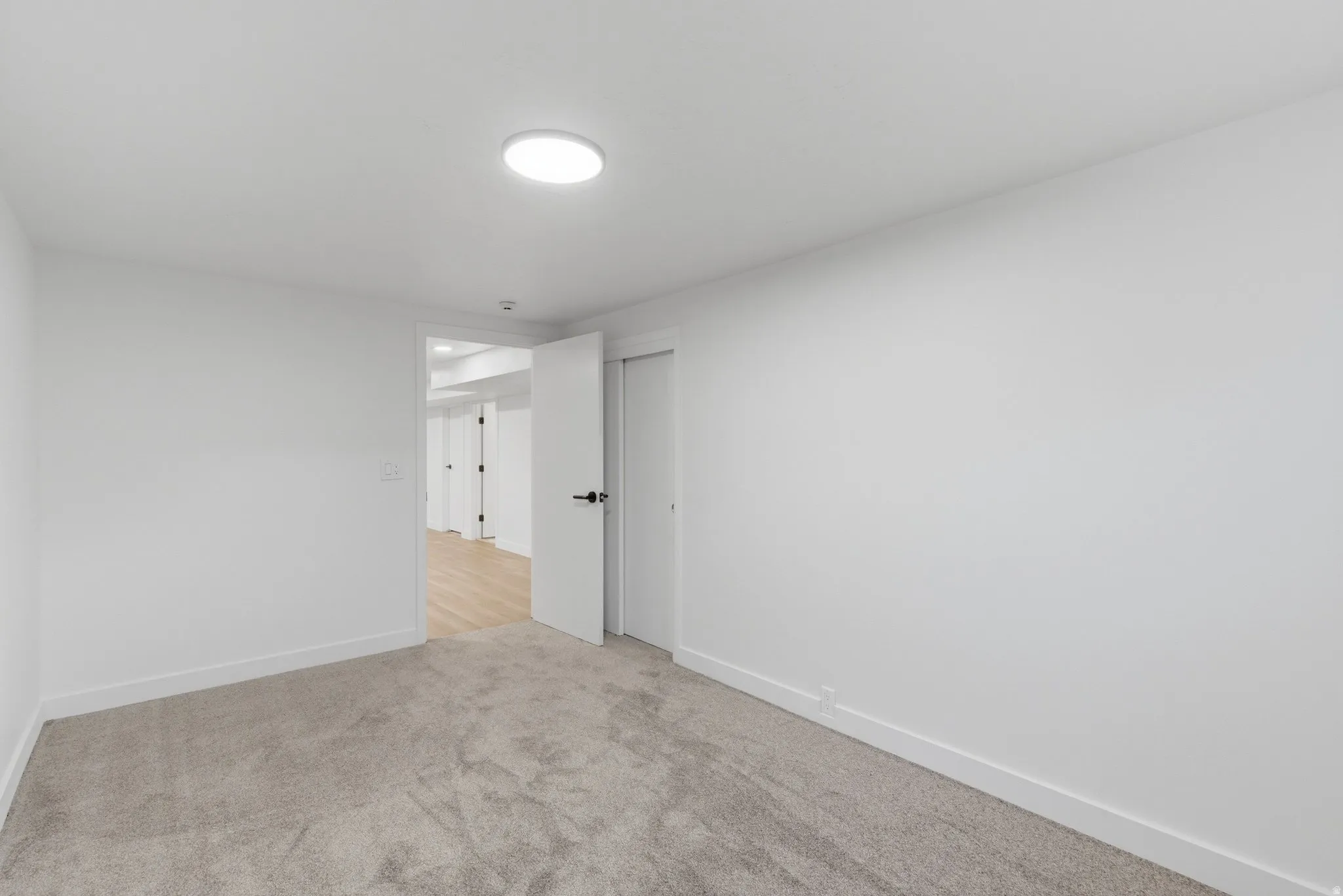 Carpeted room featuring a white door with black hardware, white baseboards, and a circular flush-mount ceiling light