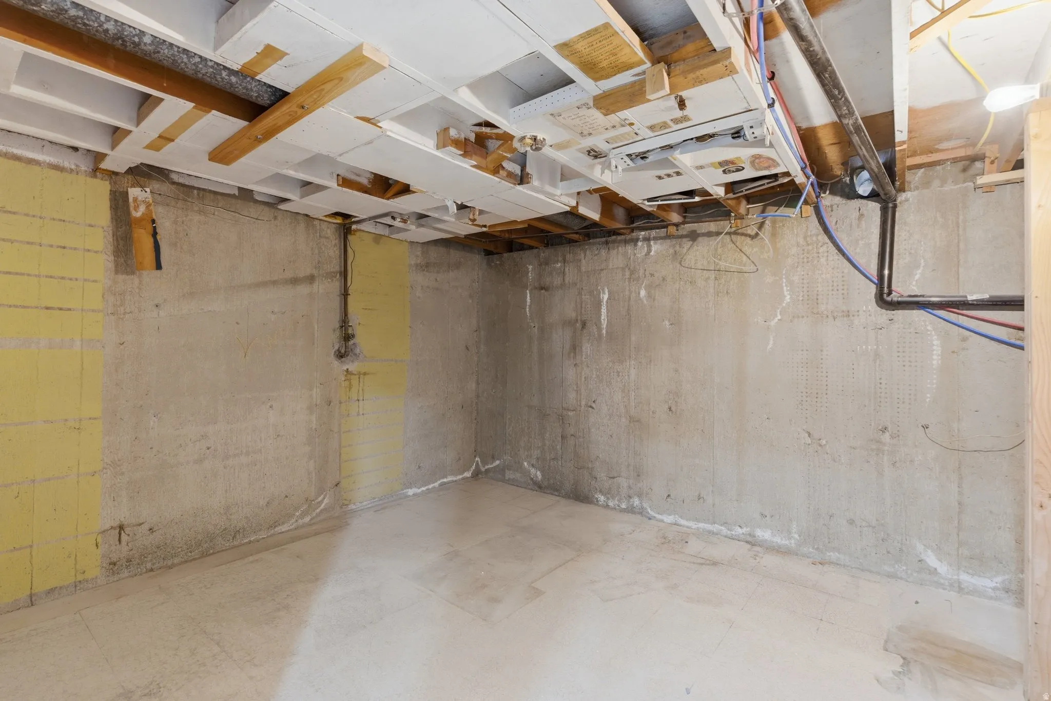 Unfinished basement featuring exposed concrete walls and flooring, open ceiling joists, and visible utility lines